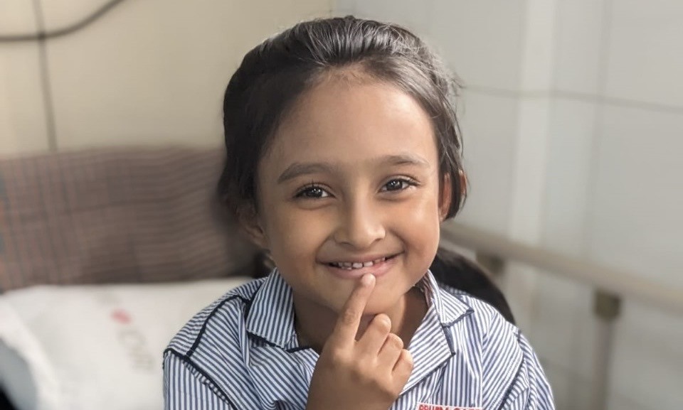 A young girl in a blue-and-white striped shirt standing in a hospital room